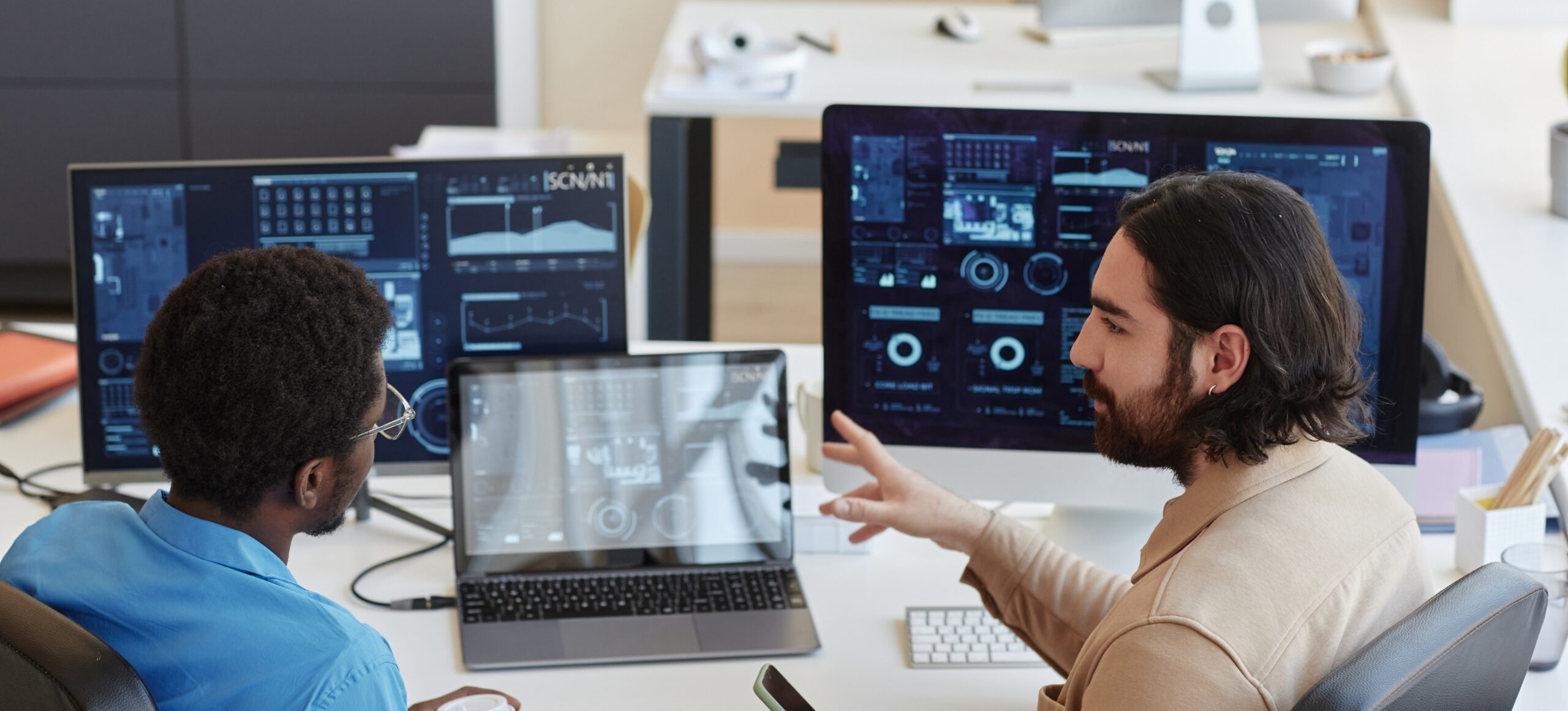 Two people sitting at a desk with two monitors